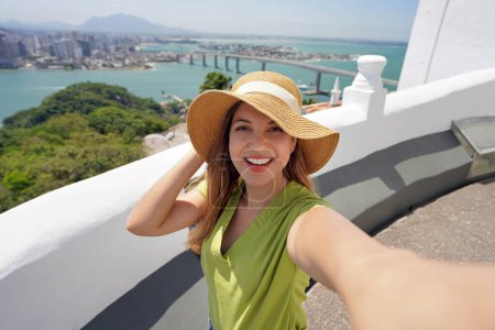 Foto de Mujer turista de moda toma selfie con vista panorámica de la ciudad de Vitoria en el estado de Espirito Santo, Brasil - Imagen libre de derechos
