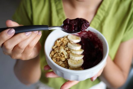 Photo for Young woman eating Brazilian acai from bowl with banana and granola as breakfast - Royalty Free Image