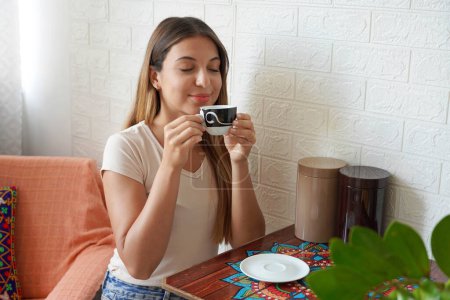 Photo for Coffee ads. Beautiful girl appreciates the smell of coffee at home. Young woman takes cappuccino in her apartment. - Royalty Free Image