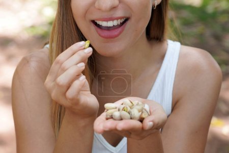 Téléchargez les photos : Fitness fille en bonne santé à l'extérieur. Gros plan d'une jeune femme mangeant des pistaches dans le parc. Focus sélectif sur sa bouche. - en image libre de droit