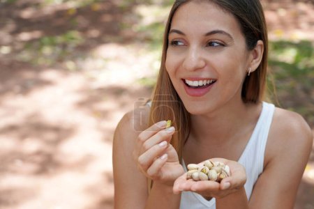 Foto de Primer plano de la atractiva mujer sana comiendo pistachos en el parque. Mira a un lado.. - Imagen libre de derechos