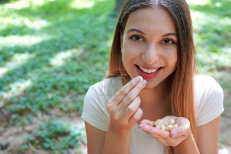 Foto de Primer plano de niña sana comiendo nueces de macadamia en el parque. Mira la cámara.. - Imagen libre de derechos