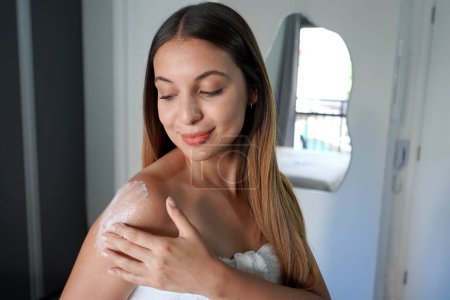 Close-up of hispanic woman applying body moisturizing lotion on her shoulder at home