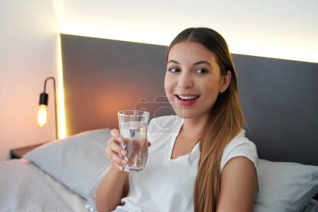 Teenager girl in the bed drinks a glass of water just woken up in the morning