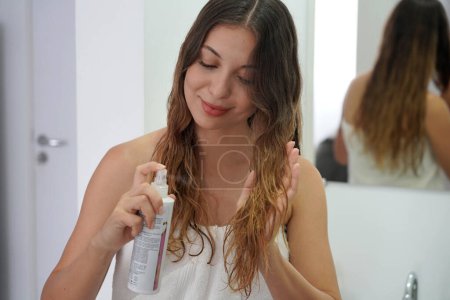 Hair Thermal Protection. Young Woman with Healthy Beautiful Long Wavy Hair Applying Thermal Protect Hair Spray. Haircare Cosmetic Thermo Protection.