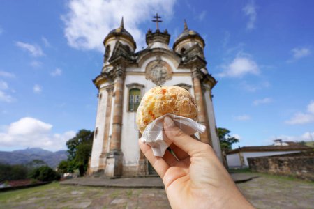 Pao de queijo (pan de queso brasileño) con la iglesia de San Francisco de Asís en Ouro Preto, Minas Gerais, Brasil, la ciudad es Patrimonio de la Humanidad por la UNESCO