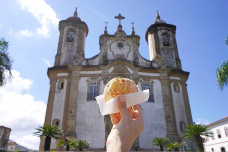 Pao de queijo (pan de queso brasileño) con la iglesia de Nuestra Señora del Monte Carmelo en Ouro Preto, Minas Gerais, Brasil, la ciudad es Patrimonio de la Humanidad por la UNESCO