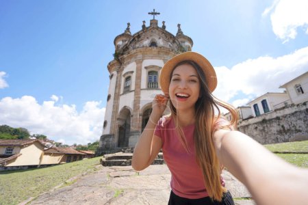 Photo for Selfie girl in Ouro Preto, Brazil. Young tourist woman taking self portrait with the church of Our Lady of the Rosary in Ouro Preto touristic destination UNESCO in Minas Gerais, Brazil. - Royalty Free Image
