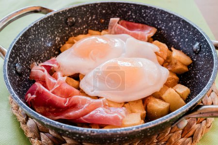 Téléchargez les photos : Œufs frits avec pommes de terre et jambon dans une casserole. Typique tapa espagnole. Photo de haute qualité - en image libre de droit