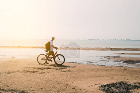 Photo for Rear view of man with backpack standing and holding bike on seafront. High quality photo - Royalty Free Image