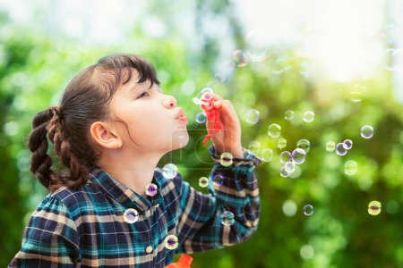 Foto de Asiático preescolar chica jugar jabón burbuja soplando juguete en playsgound con verde verano naturaleza fondo - Imagen libre de derechos