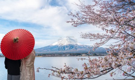 Couple traveller with a red umbrella and walking over the bridge with Fuji mountain and Sakura flower background in Tokyo city, Japan