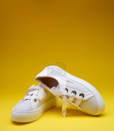 Foto de Zapatillas blancas de moda de cuero perforado con suelas de goma gruesas, aisladas sobre un fondo amarillo degradado con espacio para copiar. Fotografía moda - Imagen libre de derechos