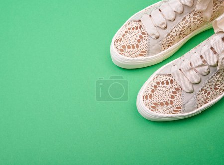 Foto de Delicado diseño de punto beige casual zapatillas femeninas sobre un fondo de papel verde con espacio para copiar. Diseño minimalista creativo con calzado. - Imagen libre de derechos