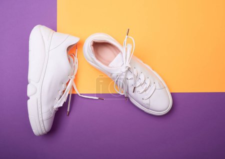Foto de Vista superior de las modernas zapatillas femeninas blancas con suelas gruesas de plataforma y detalles brillantes en cordones de zapatos, colocadas sobre un fondo púrpura-naranja. Mock-up para la publicidad de diseño para una tienda de zapatos - Imagen libre de derechos