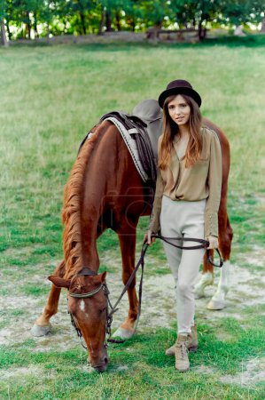 Téléchargez les photos : Jeune femme au chapeau noir avec cheval brun à la campagne. L'équitation favorise le bien-être, la relaxation. certificat cadeau pour émotion, type de culture physique thérapeutique, Hippothérapie - en image libre de droit