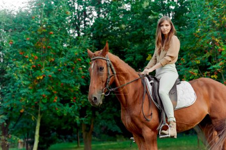 Téléchargez les photos : Formation équestre à la campagne. Jeune femme jockey chevauchant un cheval brun dans la forêt d'été. Certificat cadeau pour les émotions avec des leçons d'équitation. Hippothérapie, thérapie à cheval - en image libre de droit