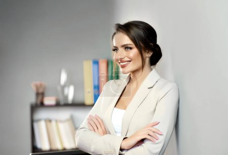 Photo for Gorgeous young woman standing with her arms crossed and smiling while looking away leaning on a gray wall at the office. Successful entrepreneur. Friendly psychologist, life coach, career consultant. - Royalty Free Image