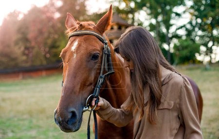 Téléchargez les photos : Une femme et son cheval dans un environnement rural, sur un terrain herbeux. Portrait d'une jeune cavalière au milieu de la nature, dressant des chevaux, et utilisant une arène extérieure simulée. Promouvoir le bien-être et le soulagement du stress. - en image libre de droit