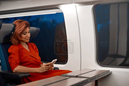 Foto de Las mujeres viajan con teléfonos inteligentes móviles en el transporte en tren, revisan sus redes sociales, leen el sitio web o la información de Internet sobre el viaje en otra ciudad. Disfrutando de tren interurbano de alta velocidad sin demora - Imagen libre de derechos