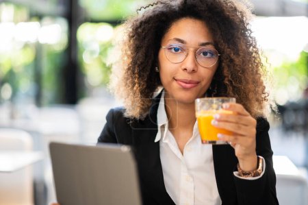 Foto de Joven mujer de negocios afroamericana usando su tableta digital en un descanso con un jugo de naranja - Imagen libre de derechos