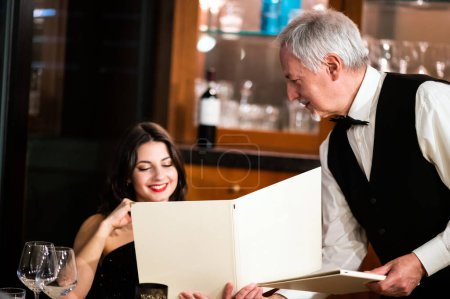 Téléchargez les photos : Waiter giving a menu to a woman in an elegant restaurant - en image libre de droit