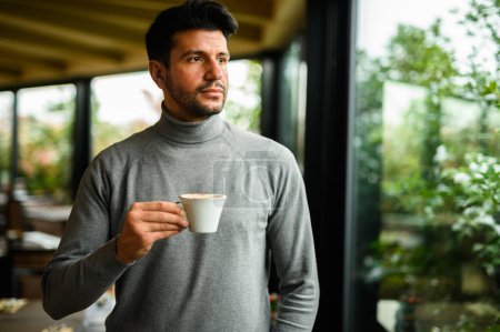 Téléchargez les photos : Young man having a coffee and looking outdise the window - en image libre de droit
