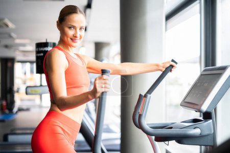 Téléchargez les photos : Woman exercising in a gym with an elliptical cross trainer - en image libre de droit