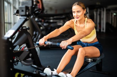 Photo for Young blonde woman working on rowing machine - Royalty Free Image