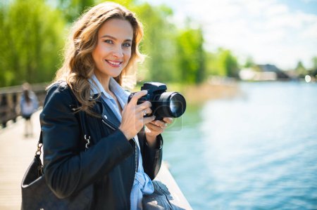 Téléchargez les photos : Jeune femme souriante tenant un appareil photo reflex extérieur - en image libre de droit