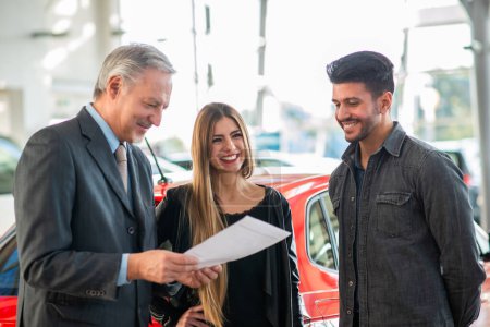 Photo for Happy young family talking to the salesman and choosing their new car in a showroom - Royalty Free Image