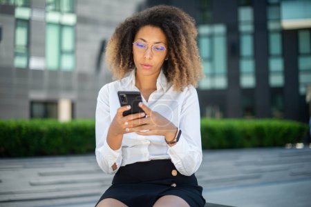 Téléchargez les photos : Portrait d'une femme d'affaires afro-américaine utilisant son téléphone portable dans un environnement professionnel - en image libre de droit