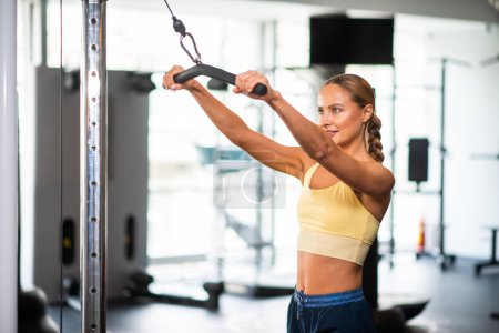 Téléchargez les photos : Femme utilisant une machine pour s'entraîner dans une salle de gym - en image libre de droit