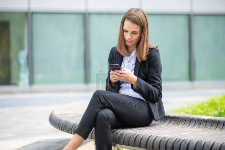 Photo for Portrait of a young woman using phone sitting on a bench outdoor - Royalty Free Image