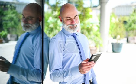 Photo for Handsome stylish bald manager using a smartphone outdoor - Royalty Free Image