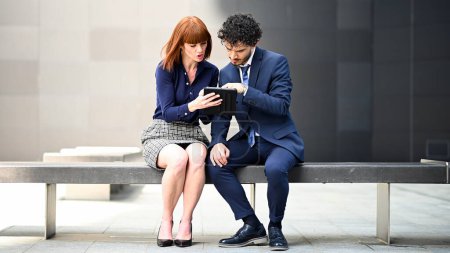 Photo for Two business colleagues using a tablet outdoor sitting on a bench - Royalty Free Image