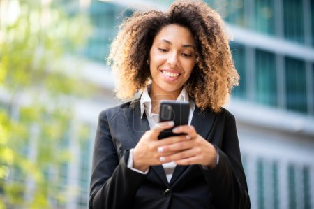 Foto de Hermosa joven mujer afroamericana gerente utilizando su teléfono inteligente al aire libre - Imagen libre de derechos