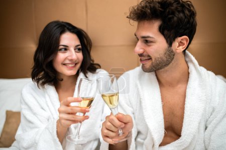 Photo for Cheerful couple in bathrobe toasting champagne glasses - Royalty Free Image