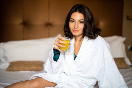 Téléchargez les photos : Portrait de belle femme en peignoir blanc buvant du jus d'orange - en image libre de droit