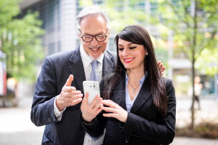 Photo for Senior manager showing something on a smartphone to his younger colleague - Royalty Free Image