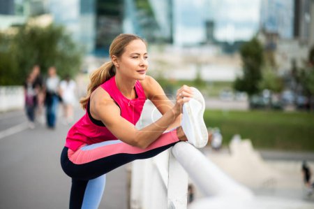 Photo for Young female runner stretching on a bridge in an urban setting - Royalty Free Image