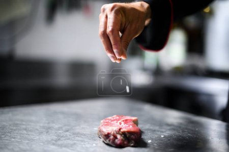 Photo for Chef pouring salt on a raw steak to season it - Royalty Free Image