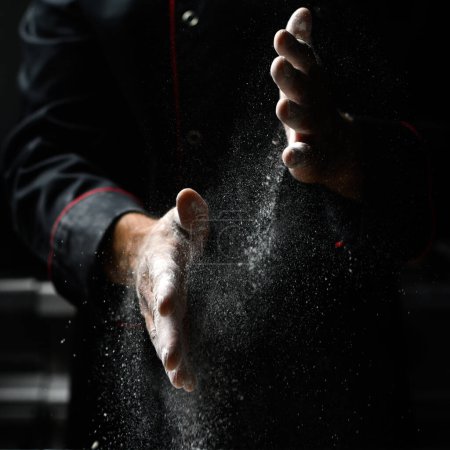 Photo for Closeup of chef's hands sprinkling flour, dark background - Royalty Free Image