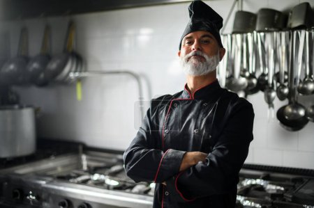 Photo for Mature chef in black coat with folded arms in his kitchen - Royalty Free Image