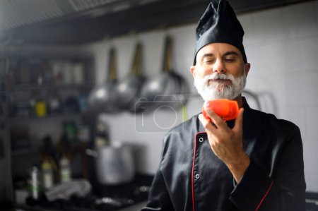 Foto de Chef profesional en uniforme negro oliendo pimienta roja - Imagen libre de derechos