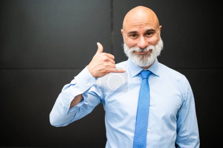 Téléchargez les photos : Mature chauve élégant portrait d'homme d'affaires avec une barbe blanche en plein air faisant l'indicatif d'appel avec sa main - en image libre de droit
