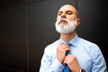 Photo for Mature bald stylish businessman portrait with a white beard outdoor adjusting his necktie - Royalty Free Image