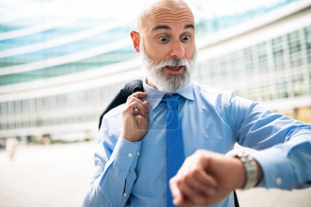 Téléchargez les photos : Homme d'affaires vérifiant sa montre-bracelet avec une expression choquée - en image libre de droit