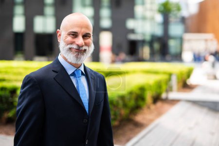Téléchargez les photos : Mature chauve élégant portrait d'homme d'affaires avec une barbe blanche en plein air dans une ville verte - en image libre de droit