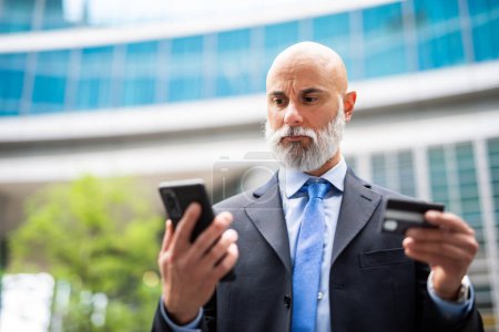 Photo for Handsome stylish bald manager using a smartphone outdoor to buy something with his credit card - Royalty Free Image